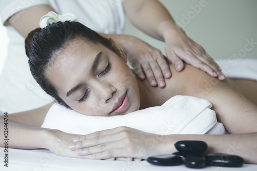 Close up of attractive young Asian woman laying and closing eyes during getting Spa treatment by therapist on white bed