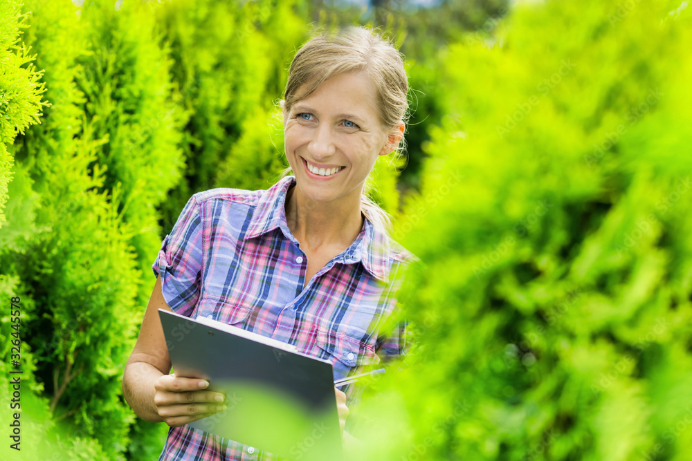 Portrait of mature owner smiling while writing report on clipboard in garden Portrait of mature owner smiling while writing report on clipboard in garden