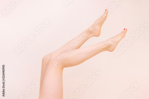 Female bare legs raise, On a beige background. Beauty salon, depilation, care, medicine, varicose veins, cosmetic surgery, spa and treatment concept.