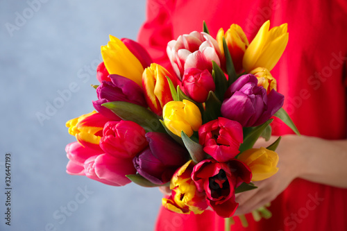 Woman holding beautiful spring tulips on light blue background, closeup