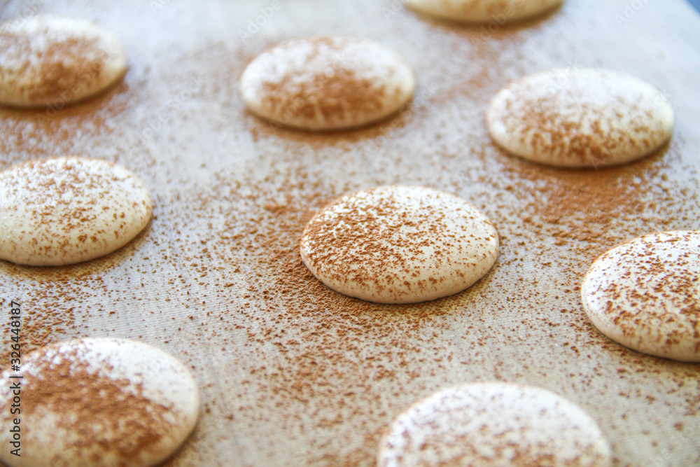 French dessert macaron. The photo of making macaron powdered with cocoa powder. Macaron in process, before baking. Macarons piped on a tray covered with a teflon sheet. Back view. French dessert macaron. The photo of making macaron powdered with cocoa powder. Macaron in process, before baking. Macarons piped on a tray covered with a teflon sheet. Back view.