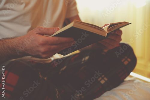 Young man reading book on bed at home, closeup
