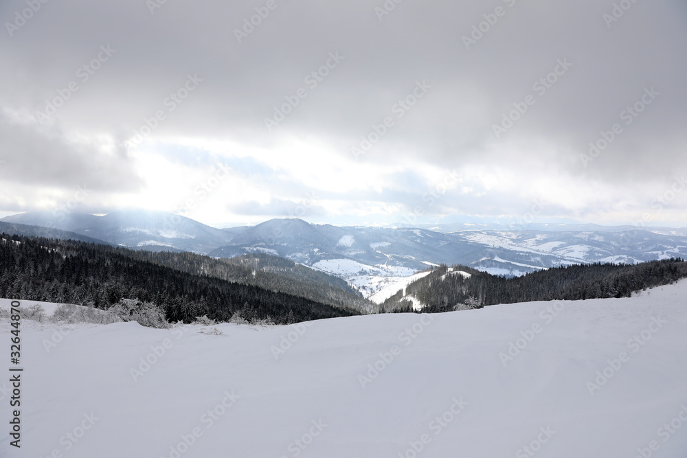 Picturesque mountain landscape with snowy hills under cloudy sky