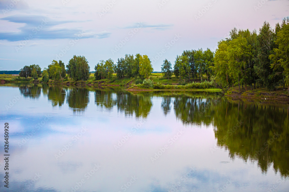 classic nature landscape with clear lake, green grass and few trees