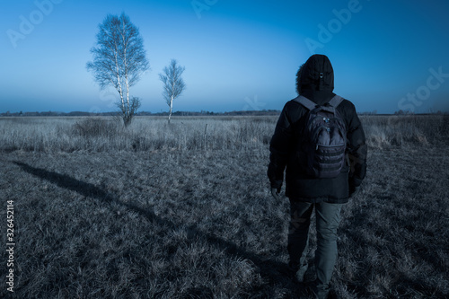 Male traveler with a backpack walking across the meadow in the morning, Nowiny, Poland
