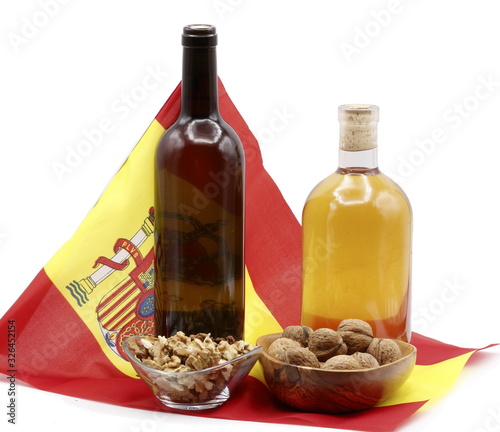 products from Spain, Advertising photo with bottle of Galician white wine, bottle of sweet mistela, glass bowl with unpeeled pine nuts, olive wood bowl with nuts, on flag of Spain, white background. photo