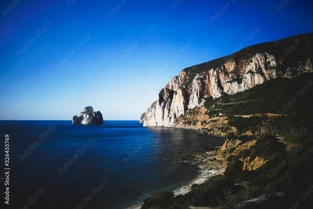 Fototapeta premium Panoramic view of the coast line with a sugar loaf monumental rock and a cliff falling into the sea in a bright sunny day.