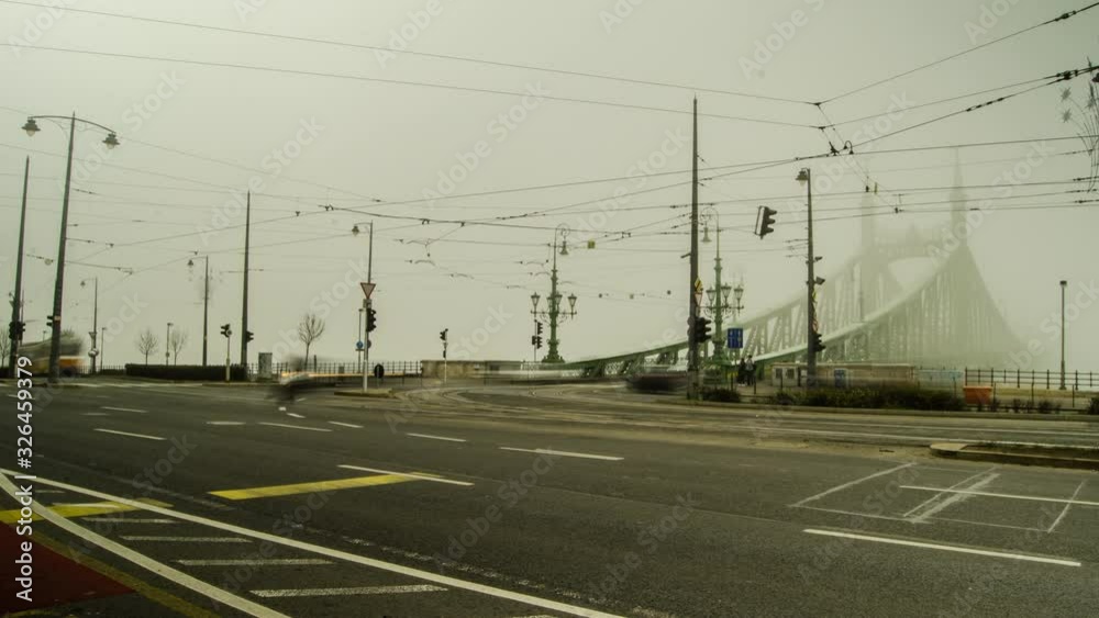 BUDAPEST – Timelapse of Liberty Bridge traffic on a foggy winter day with cars and trams in view BUDAPEST – Timelapse of Liberty Bridge traffic on a foggy winter day with cars and trams in view
