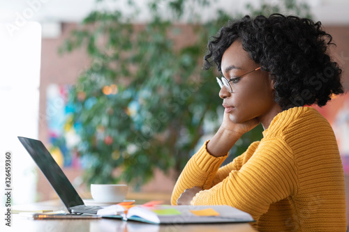 Plakat Pensive afro girl editor reading text on laptop