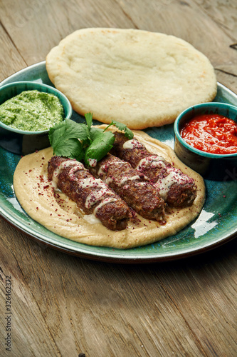 Appetizing rolls of Lyulya kebab - cooked over a lamb minced meat with a side dish of hummus with pita and salsa on ceramic plate. Vertical, wooden background, Eastern cuisine photo