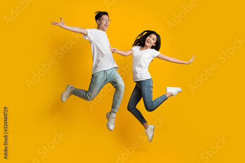 Emotional asian couple jumping over yellow background