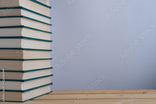 A stack of books with a green cover lying on a wooden table and depicted on a light gray background in the style of minimalism.