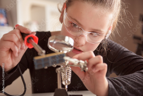 Little girl with safety glasses works with a soldering iron on a computer component