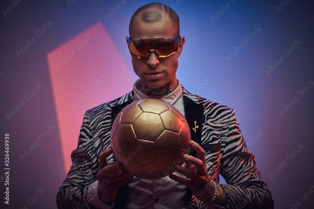 Plakat Stylish, handsome, tattooed, bald male model posing in a studio for the photoshoot wearing fashionable custom made zebra striped style tuxedo, glasses and rose patterned shirt, looking on a golden