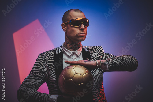 Plakat Fashionable, handsome, tattooed, bald male model posing in a studio for the photoshoot wearing fashionable custom made zebra striped style tuxedo, glasses and rose patterned shirt, looking on a golden