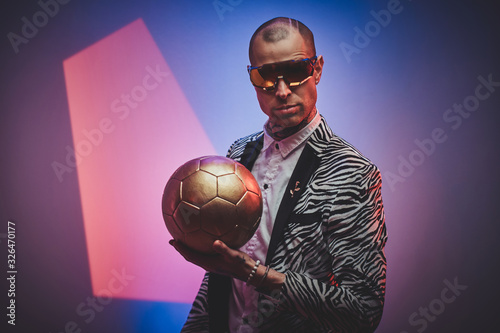 Plakat Beautiful, daring, tattooed, bald male model posing in a studio for the photoshoot wearing fashionable custom made zebra striped style tuxedo, glasses and rose patterned shirt, looking on a golden
