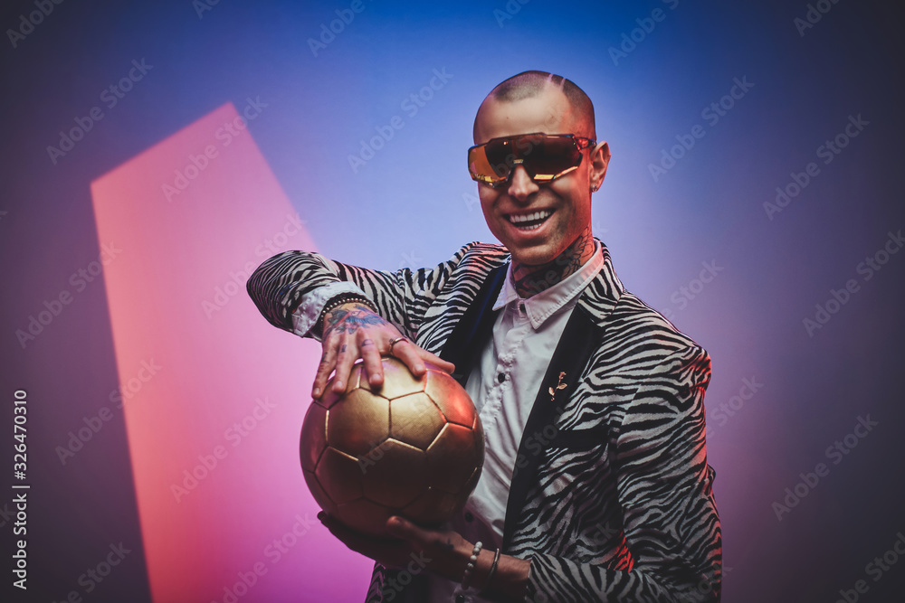 Plakat Fashionable, elegant, tattooed, bald male model posing in a studio for the photoshoot wearing fashionable custom made zebra striped style tuxedo, glasses and rose patterned shirt, looking on a golden