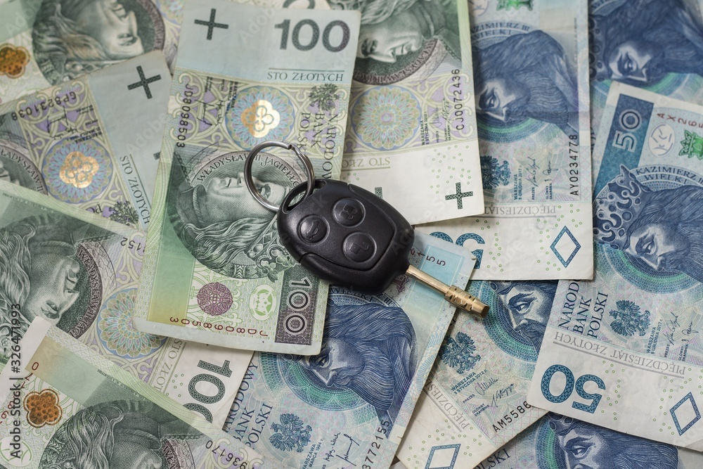 Kluczyki do samochodu leżą na pieniądzach. Gotówka w polskich złotych leży na stole.