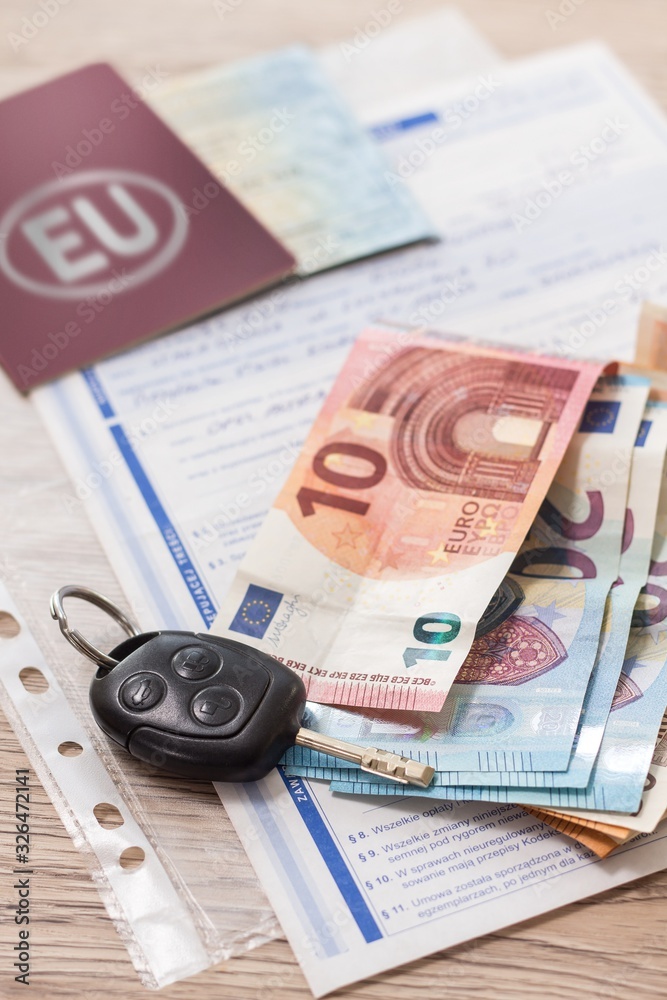 Umowa zakupu auta leży na stole. Banknoty Euro i kluczyki leżą na dokumentach zakupu.