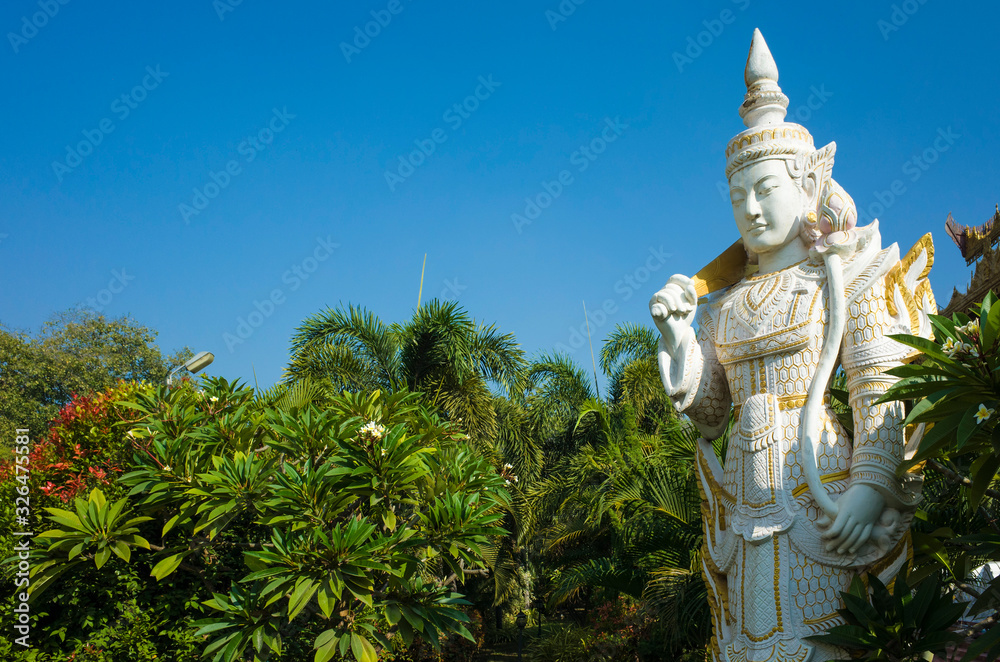 White sculpture of Spirit (Nat) guard surrounded by tropical trees at Kyauktawgyi Pagoda complex in Mandalay, Myanmar