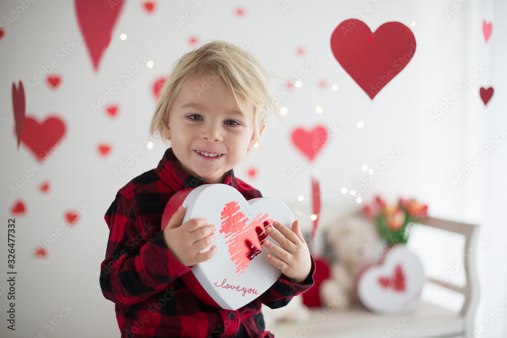 Cute blonde toddler boy, holding box in heart shape and flowers Cute blonde toddler boy, holding box in heart shape and flowers