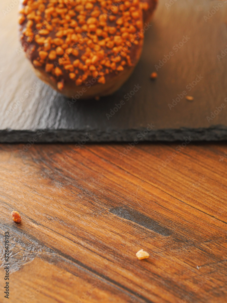 Crumb on a wooden table in focus, chocolate doughnut out of focus in the background.