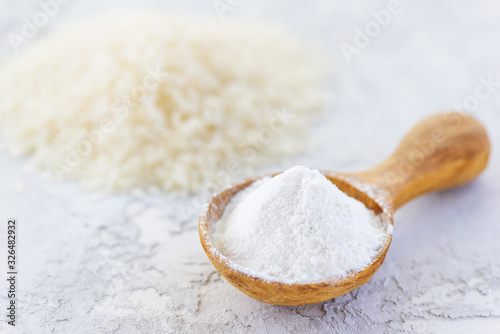 Rice flour in a wooden spoon on a gray table. Gluten free, healthy diet concept. photo