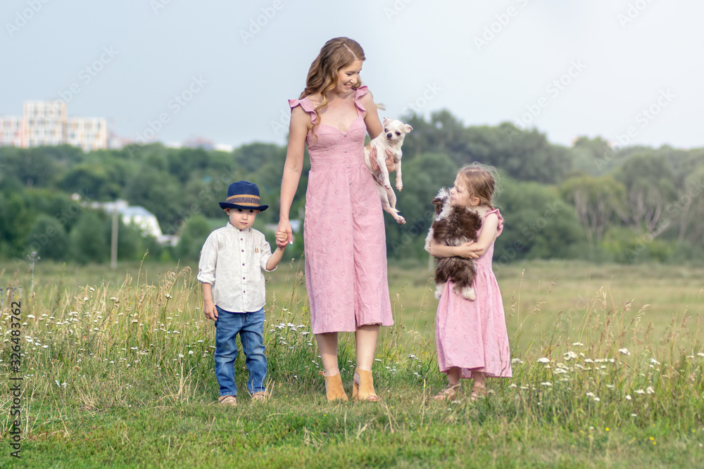 happy family outdoors on the grass in a park. mom and two children with two little dogs happy family outdoors on the grass in a park. mom and two children with two little dogs