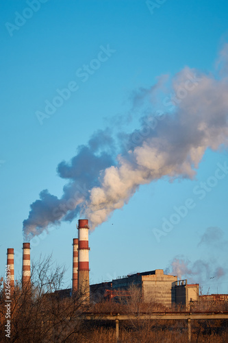 The plant emits smoke and smog from the pipes during a sunny day, pollutants enter the atmosphere. Ecological catastrophy. Harmful emissions. Chemical industry