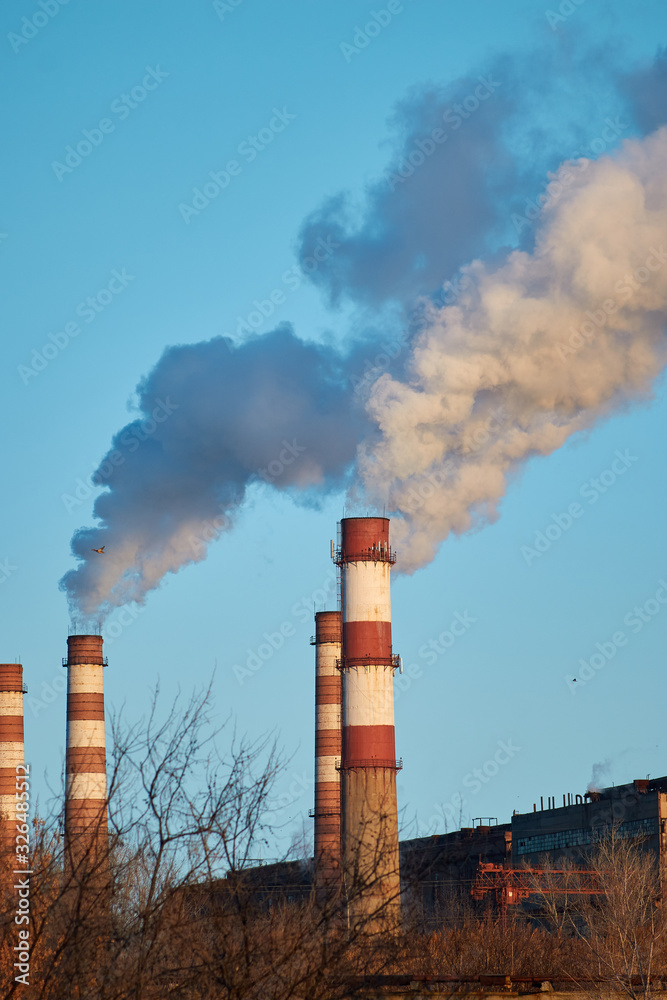 The plant emits smoke and smog from the pipes during a sunny day, pollutants enter the atmosphere. Ecological catastrophy. Harmful emissions. Chemical industry