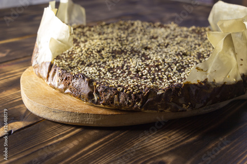 Freshly baked homemade amaranth bread sprinkled with sesame seeds. Hot bread in baking paper, lies on the kitchen board on a wooden table. Only from the oven. Natural healthy food. Selective focus