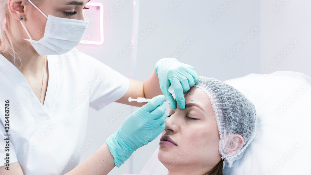 The young beautician doctor preparing to making injection in female forehead. The doctor cosmetologist makes anti-aging treatment and face lift procedure. The young beautician doctor preparing to making injection in female forehead. The doctor cosmetologist makes anti-aging treatment and face lift procedure.