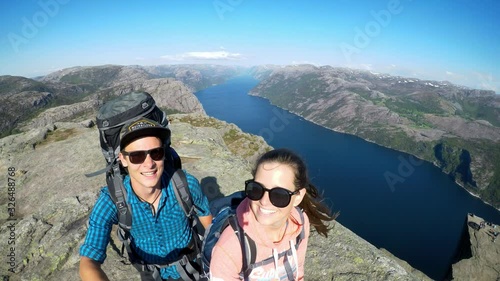A hiking couple standing at the edge of Preikestolen, Norway. They are jumping around, enjoying their time, having fun while travelling. Beauty of the nature. Lysefjord behind them going far inside