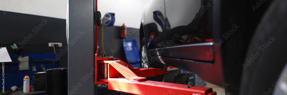 Naklejka premium Close-up of red pillaring stand used for automobiles and sportcars examinations and lifting heavy machinery. Hardworking people mechanics repair differential and engines indoors
