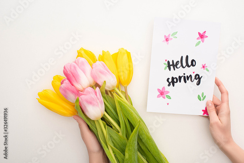 Cropped view of woman holding bouquet of tulips and card with hello spring lettering on white background