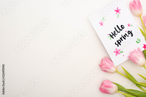 Fototapeta Naklejka Na Ścianę i Meble -  Top view of card with hello spring lettering and tulips on white background