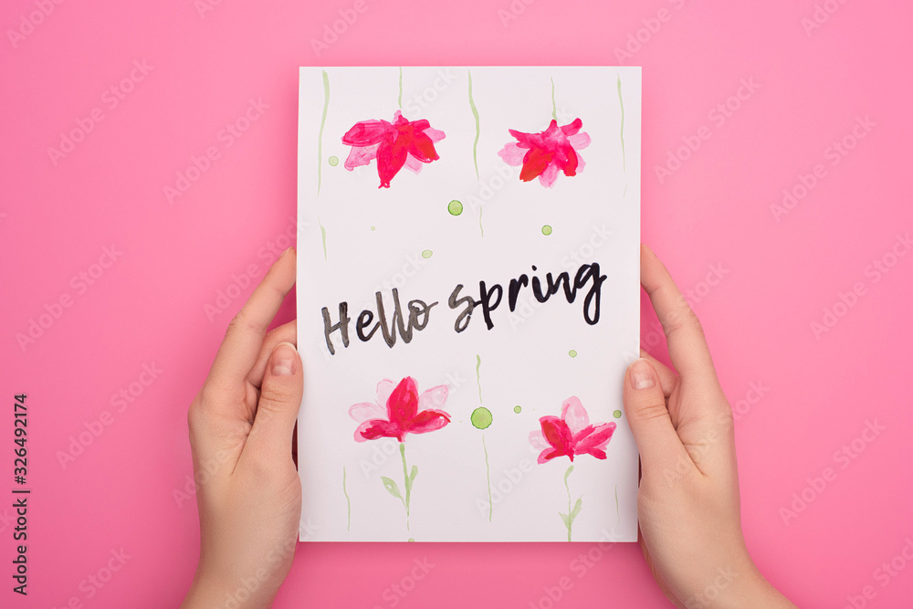 Cropped view of woman holding card with hello spring lettering on pink background Cropped view of woman holding card with hello spring lettering on pink background