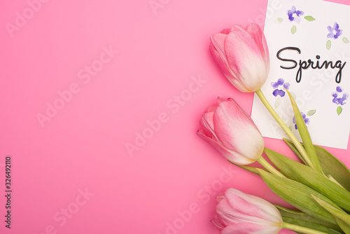 Fototapeta Naklejka Na Ścianę i Meble -  Top view of tulips and card with spring lettering on pink background