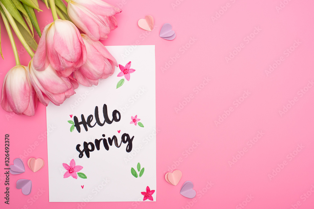 Top view of tulips, card with hello spring lettering and decorative hearts on pink