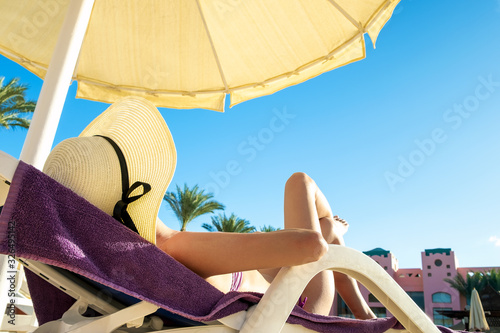 Young woman relaxing outdoors on sunny summer day. Happy lady lying down on comfortable beach chair sunbathing. Calm girl in straw hat enjoying fresh air relaxing.