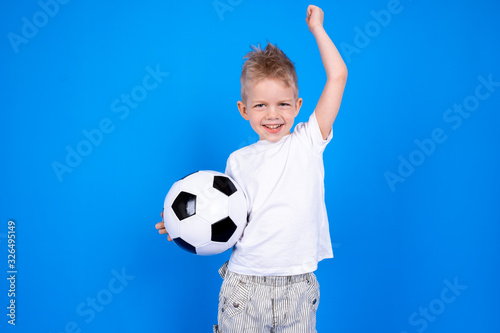 Soccer fans. Cheerful caucasian child boy boy celebrating victory holding soccer ball in hands over blue studio background. Copyspace. Football game © Наталия Кузина