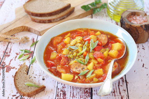 Spicy pea soup with potatoes, tomatoes, sausages and slices of bread