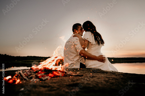 Young couple embracing and kissing on Sunset coast near the fire. Romantic love story.
