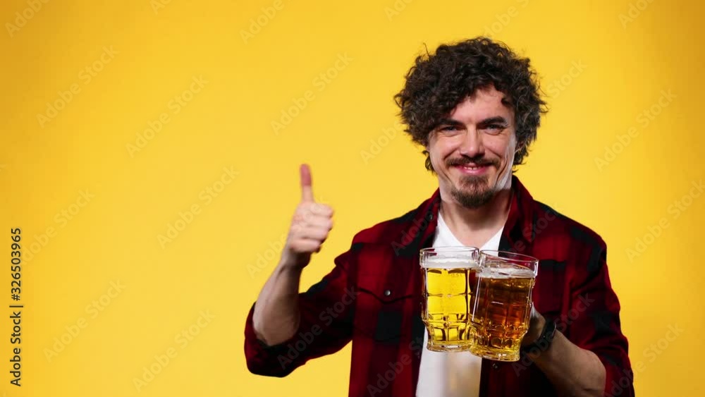 Saint Patrick Day. Young Oktoberfest man serving big beer mug with drink isolated on yellow background. Guy showing thumbs up sign with fingers. Saint Patrick Day. Young Oktoberfest man serving big beer mug with drink isolated on yellow background. Guy showing thumbs up sign with fingers.