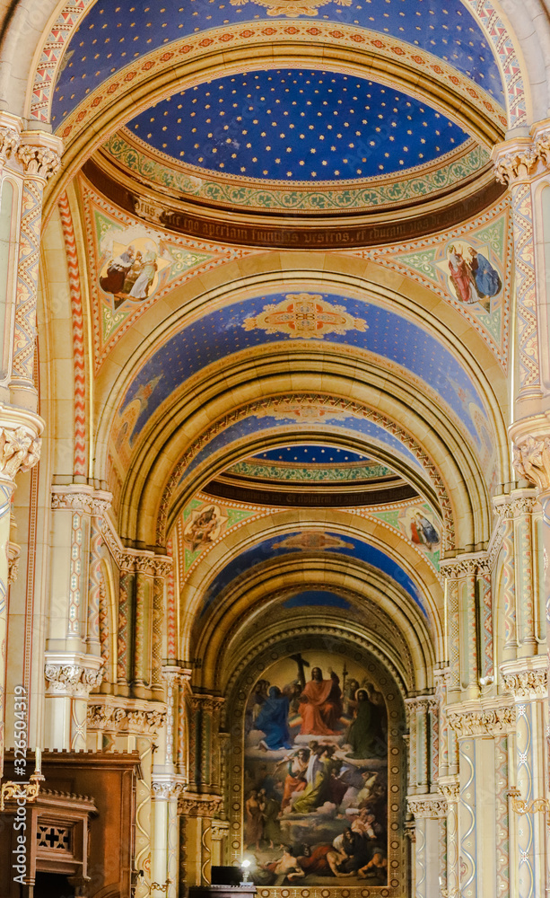 Interior stone corridor of a church with blue vaults and a painting in the background.