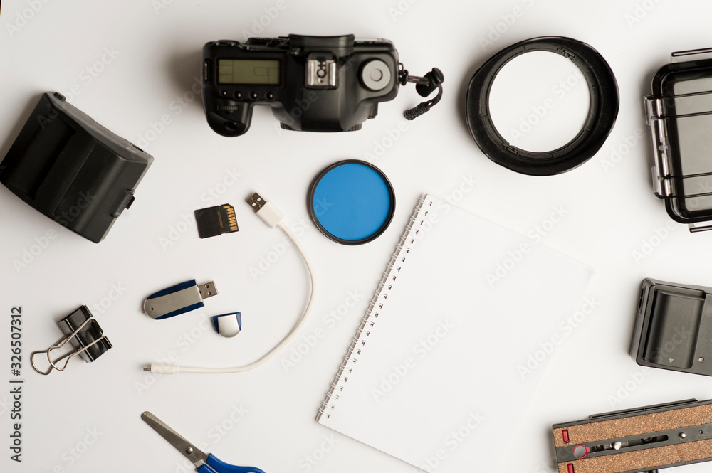 Flat assembly composition with photographic production equipment, with writing book, and accessories, on plain white background, top view