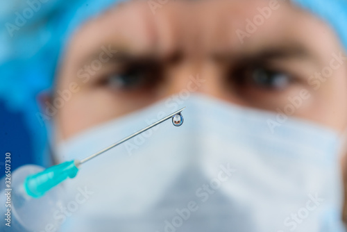 Professional doctor with medical syringe in hands ready for injection. Doctor with syringe is preparing for injection. Doctor in gloves and medical mask holds syringe with vaccine. Injection. Closeup.