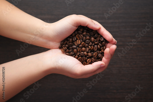 coffee beans in female hands on dark textured background