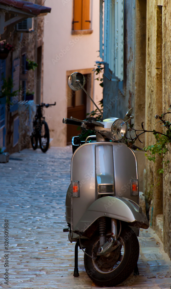 An old silver moped parled on a narrow pawed street in Italy.