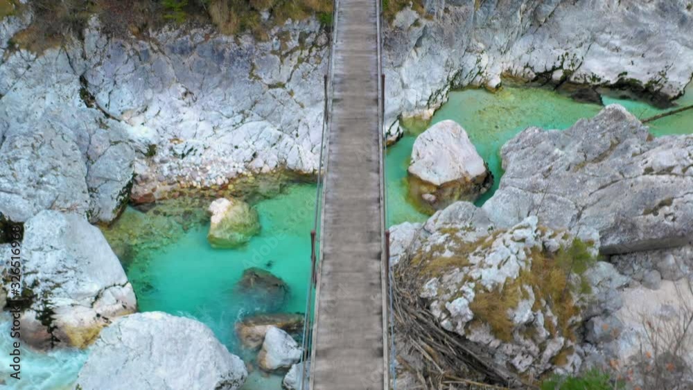 Close up the aerial view over the upstream river Soca and suspension bridge in the mountain valley. Close up the aerial view over the upstream river Soca and suspension bridge in the mountain valley.